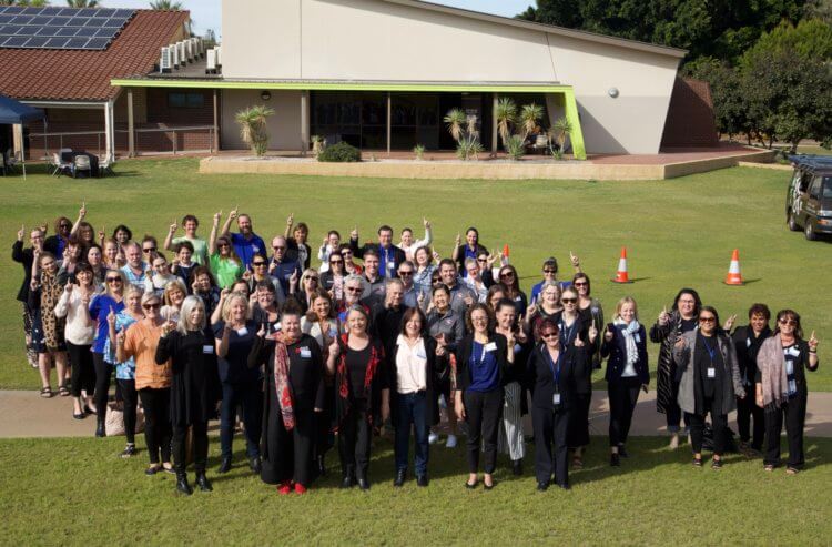 Attendees of the Community Respect & Equality Summit standing together on a grass overall together showing their unity to prevention of family violence in Geraldton