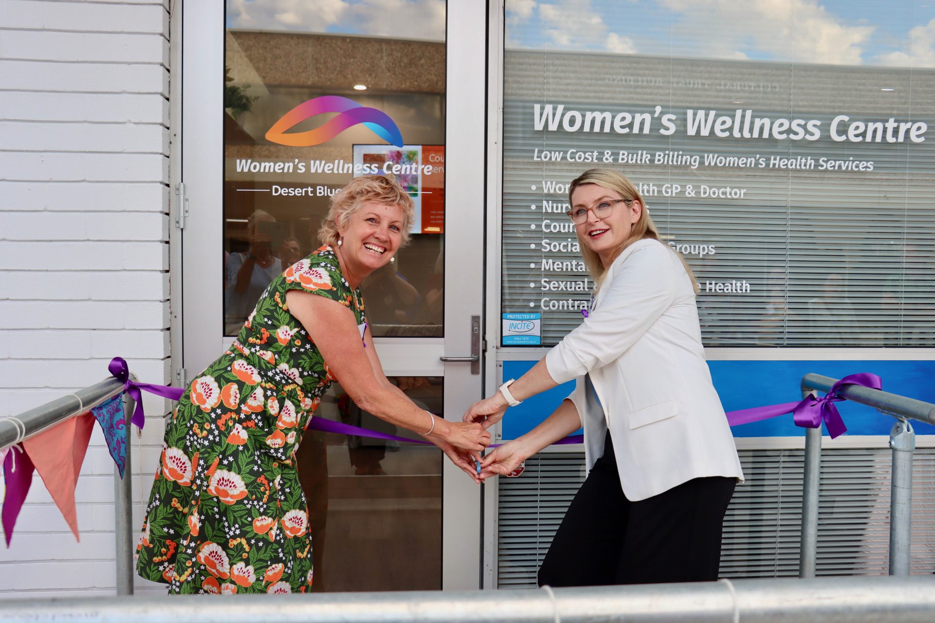 Two women, Lara Dalton and Sandra Carr, cutting a ribbon in front of a women's wellness centre.
